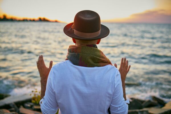 Individual looking upon ocean with palms raised